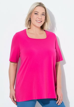 Maglietta rosa a maniche corte con scollo quadrato. Realizzata in tessuto morbido, presenta una vestibilità comoda e spacchetti laterali, abbinata a pantaloni blu.