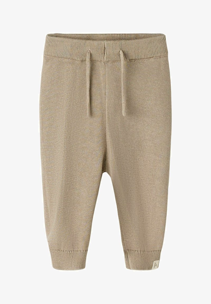 Beżowe dzianinowe spodnie dla niemowląt z prążkowanym pasem i mankietami, wyposażone w regulowany sznurek oraz małą materiałową etykietę na mankiecie.