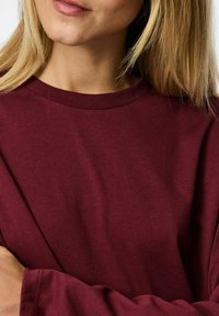 Bordowa bluzka z długim rękawem i okrągłym dekoltem, wykonana z miękkiej bawełny, o gładkiej fakturze i luźnym kroju.