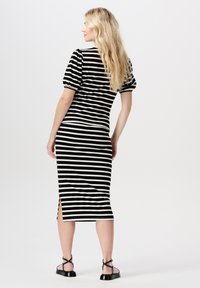 Stribet strikkjole i sort og hvid med en tætsiddende silhuet, korte puffærmer og sideslids. Båret med sorte stroppesandaler.