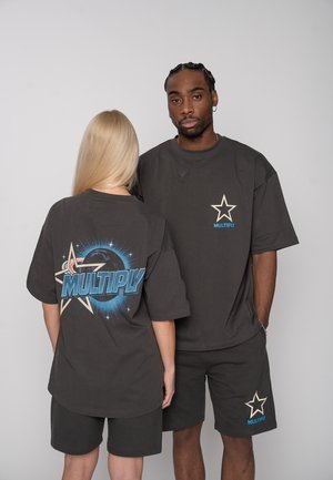 Two people wearing black matching shorts and T-shirts with blue star and "MULTIPLY" logos, one facing forward, the other showing a back design.