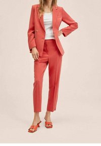 Coral pant suit with a double-breasted blazer and slim-fit trousers. Paired with orange slide sandals, displayed against a neutral background.