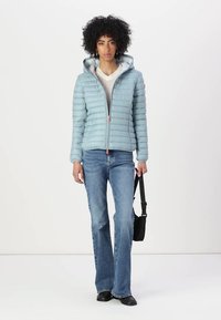 Lichtblauw pufferjack met horizontale quilting, ritssluiting en een capuchon. Gecombineerd met flared jeans en een zwarte schoudertas.