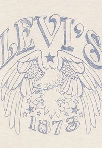 Levi's kremfarget skjorte med blå grafisk design av en ørn med vinger, stjerner og året "1873" i en fet skrifttype.