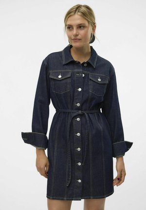 Jeansklänning i mörkblått med knäppning fram, två bröstfickor och bälte i midjan. Har kontrasterande gula sömmar och manschetter.