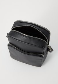 Fekete bőrtáska két cipzáros rekesszel, texturált felület, ezüstszínű cipzárok, téglalap alakú és minimalista dizájn.