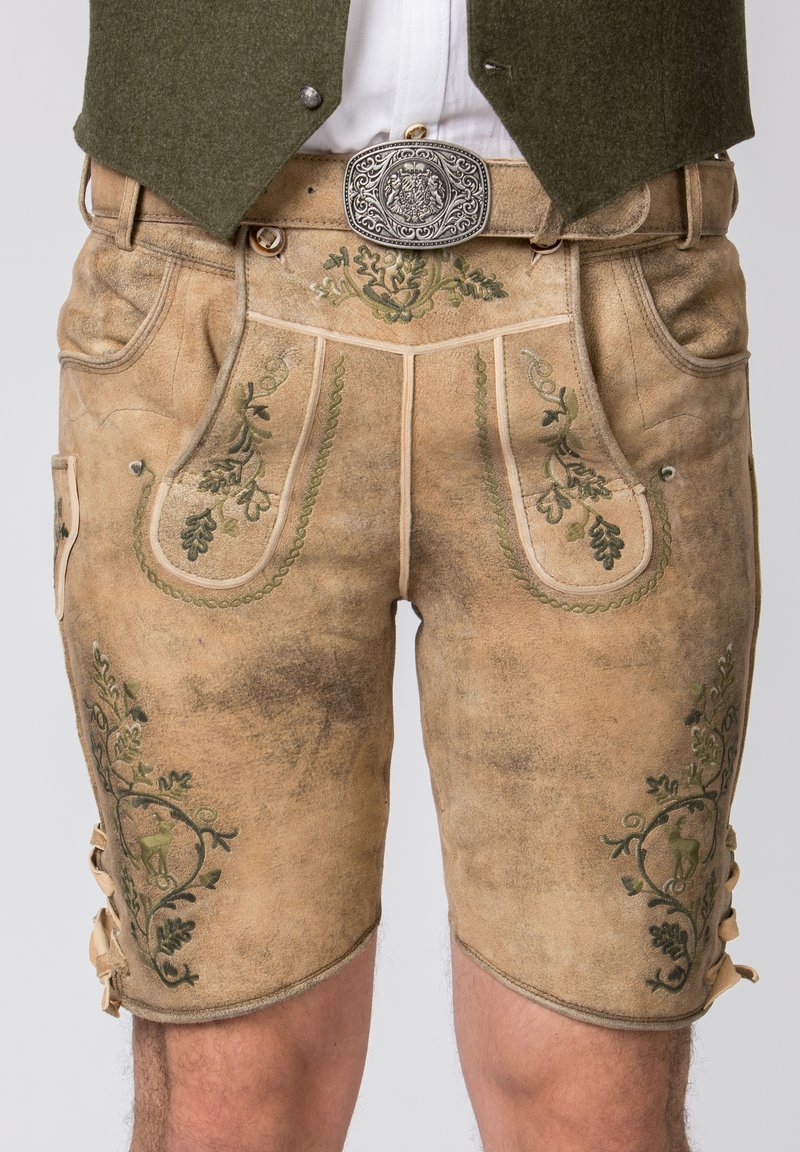 Shorts traditionnels en cuir tan, ornés de broderies florales vertes, avec poches latérales et lacets décoratifs sur les côtés. Détail de boucle en argent.