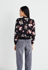 Sweatshirt noir à fleurs avec des fleurs roses et blanches, avec des poignets et ceinture côtelés ; associé à un jean gris taille haute.
