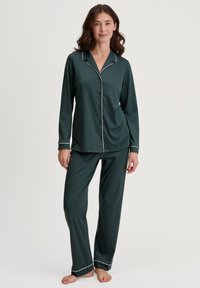 Waldgrünes Pyjama-Set aus weichem Stoff; verfügt über lange Ärmel, eine Knopfleiste vorne und weiße Paspelierungen an Kragen und Säumen.