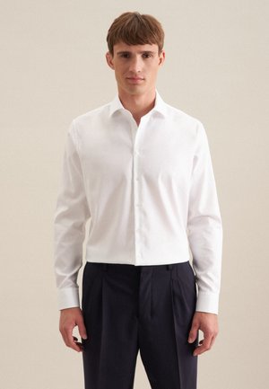 Weißes Langarmshirt mit einem Umlegekragen und durchgehender Knopfleiste. Getragen mit navyfarbenen Hosen. Glatte Textur und taillierte Passform.