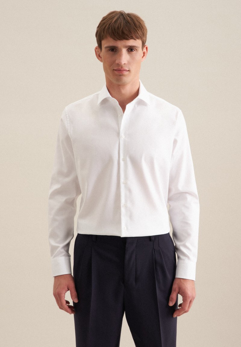 Weißes Langarmshirt mit einem Umlegekragen und durchgehender Knopfleiste. Getragen mit navyfarbenen Hosen. Glatte Textur und taillierte Passform.