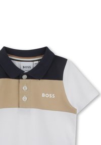 Poloshirt in marineblauw, beige en wit. Beschikt over een effen kleurontwerp, korte mouwen, een drieknoopsluiting en een logo op de borst.