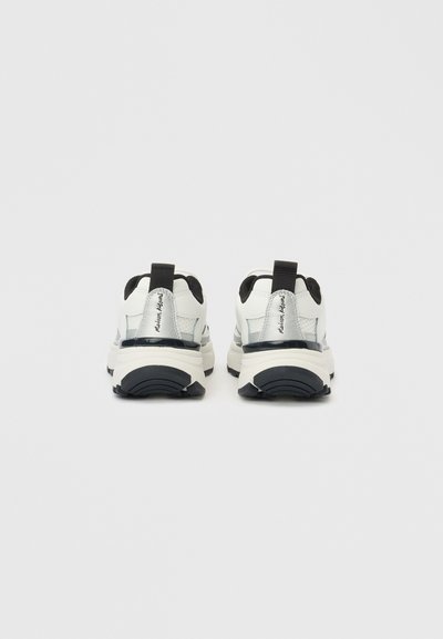 Λευκά αθλητικά παπούτσια με μαύρες λεπτομέρειες, με ανάγλυφη συνθετική επάνω επιφάνεια, θηλιά στο πίσω μέρος και μαλακή σόλα με ξεχωριστό πέλμα.