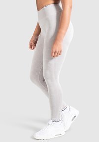 Leggings a vita alta di colore grigio chiaro, realizzati in un tessuto elastico, con una sottile texture e una vita a coste, abbinati a scarpe da ginnastica bianche.