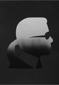 Czarny T-shirt z monochromatycznym gradientowym grafiką przedstawiającą profil z okularami przeciwsłonecznymi, gładkimi włosami i detalem kołnierzyka. Miękka bawełniana tekstura.