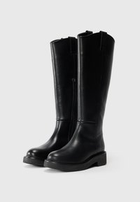 Bottes en cuir noires arrivant au genou avec une texture lisse, fermeture éclair sur le côté et semelle épaisse. Design simple avec un bout rond et une languette.