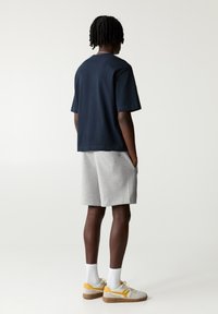 Marinefarbener kurzärmeliger T-Shirt, graue Shorts und beige-gelbe Sneaker. Das T-Shirt hat eine lässige Passform; die Shorts verfügen über seitliche Taschen und eine weiche Textur.