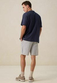 T-shirt en coton bleu marine, short rayé bleu et blanc, design décontracté, porté avec des chaussures beiges et des chaussettes claires, vu de dos.