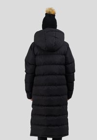 Schwarze Pufferjacke mit Kapuze, mit einem gesteppten Design und einem mittellangen Schnitt. Eine gerippte schwarze Mütze mit einem hellbraunen Pompon oben.