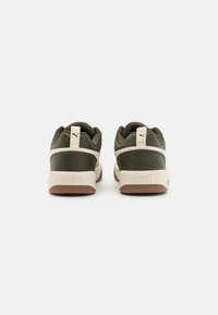 Sneaker in pelle verde con intersuola color crema e suola in gomma marrone. Presentano strisce decorative bianche e un piccolo logo sul tallone.