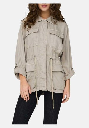 Chaqueta utilitaria beige con dos bolsillos frontales con solapa, cintura ajustable con cordón, mangas enrolladas y tejido ligero.