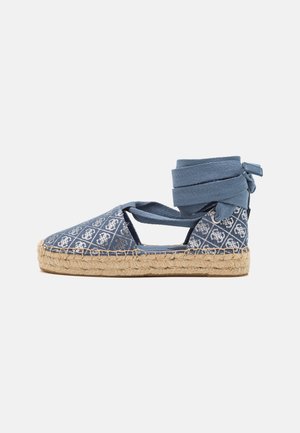 Blå espadrille med mønstret canvasoverdel, naturlig jutesål og snørebånd, der svøber omkring anklen. Åbne sider og rund tå design.