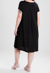 Czarna sukienka o krótkich rękawach, o luźnym kroju, sięgająca do kolan, wykonana z teksturowanej tkaniny, z centralnym zakładką z tyłu. Połączona z jasnoróżowymi sneakersami.