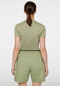 Ljust olivgrön teknisk tyg-t-shirt med korta ärmar, kombinerad med matchande shorts med svart elastiskt midjeband och perforerat mönster.