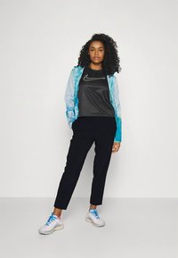 Sportos öltözék, amely könnyű, kék árnyalatú kabátot, fekete Nike pólót, fekete nadrágot és világosszürke, kék részletekkel díszített sportcipőt tartalmaz.