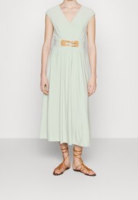 Světlounce zelené šaty ke kolenům s krátkými rukávy, výstřihem do V a staženým pasem, doplněné béžovým páskem s dvojitými sponami. Nosené s béžovými gladiátorskými sandály.