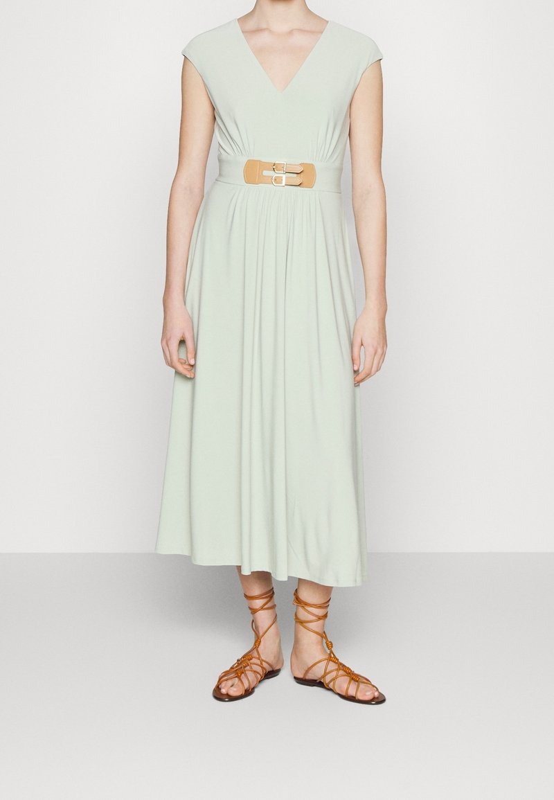 Světlounce zelené šaty ke kolenům s krátkými rukávy, výstřihem do V a staženým pasem, doplněné béžovým páskem s dvojitými sponami. Nosené s béžovými gladiátorskými sandály.