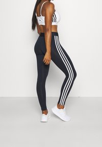 Navy leggings with three white vertical stripes along the outer sides, paired with a white sports bra. Smooth, stretchy fabric.