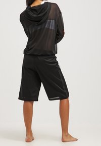 Sudadera de malla negra con capucha ajustable, combinada con pantalones cortos de malla negra sueltos. Ambas prendas presentan un acabado texturizado y un corte relajado.