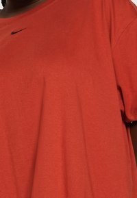 Röd bomullströja med rund hals, korta ärmar och en liten svart Nike-logotyp på vänster bröst. Mjuk, avslappnad design.