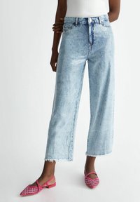 Vaaleansiniset leveät farkut, joissa on tekstuuri ja revitty helma, yhdistetty pinkkeihin palmikkokenkäisiin, joissa on terävä kärki.