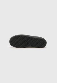 Semelle de sneaker noire avec une surface texturée présentant un motif en grille pour une meilleure traction. Talon arrondi et bord latéral pour la stabilité.