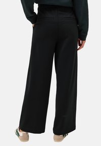 Schwarze, weit geschnittene Hose mit elastischem Bund, die über zwei Gesäßtaschen und einen glatten, dehnbaren Stoff verfügt. Kombiniert mit lässigen Sneakers.