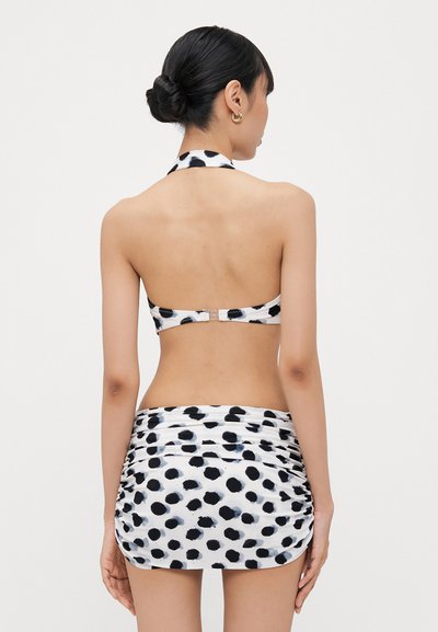 Black and white polka dot halter neck bikini top with a clip closure, paired with a mini skirt featuring gathered sides and similar pattern.