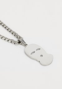 Zilveren ketting met een gepolijste metalen hanger in de vorm van een gestileerd gezicht met twee ooguitsparingen en een rond mondgat.