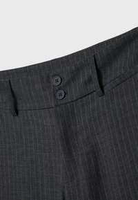 Pantalon gris foncé à fines rayures avec fermeture double à boutons noirs et passants de ceinture à la taille.