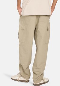 Beige cargobroek met grote zijzakken, een losse pasvorm, en een gestructureerde stof. Draag met een neutraal gekleurde shirt en lichte sneakers.