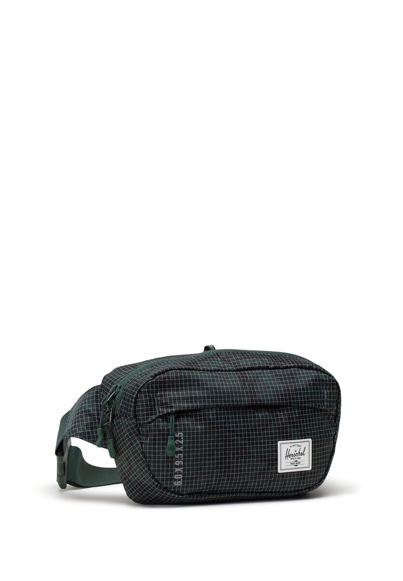 Sac banane en tissu à carreaux verts avec un compartiment principal zippé, une poche avant et une sangle réglable. Arbore le logo de la marque Herschel.