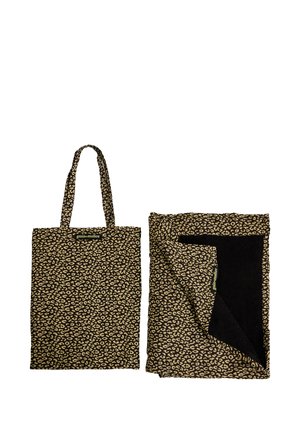 Sac fourre-tout imprimé léopard marron et noir avec poignées à côté d'une couverture pliée assortie montrant une doublure intérieure noire.