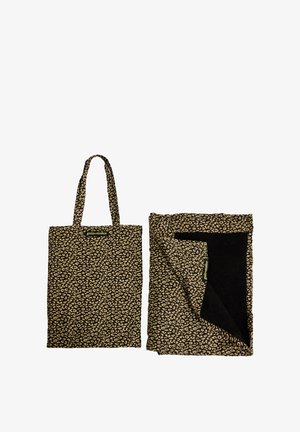 Sac fourre-tout imprimé léopard marron et noir avec poignées à côté d'une couverture pliée assortie montrant une doublure intérieure noire.
