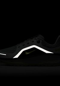 Scarpa sportiva nera con una texture trapuntata, caratterizzata da un design geometricamente bianco e un logo Nike swoosh verde scuro. Suola e lacci neri.