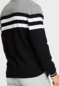 Pull-over avec une partie supérieure grise et une partie inférieure noire ornée de larges rayures blanches. Confectionné en tissu tricoté, avec des poignets côtelés.