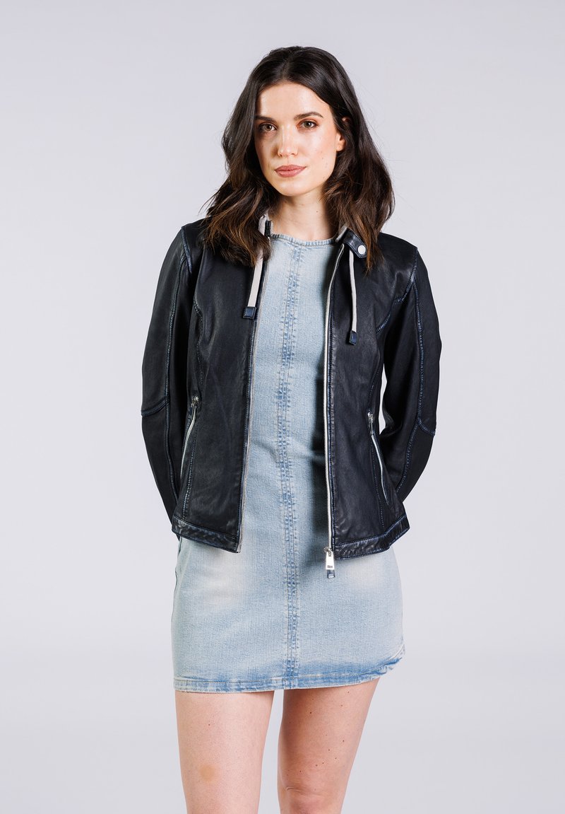 Schwarze Lederjacke mit Reißverschluss und Kordelzügen, kombiniert mit einem hellblauen Jeanskleid. Glatte Textur und figurbetontes Design.
