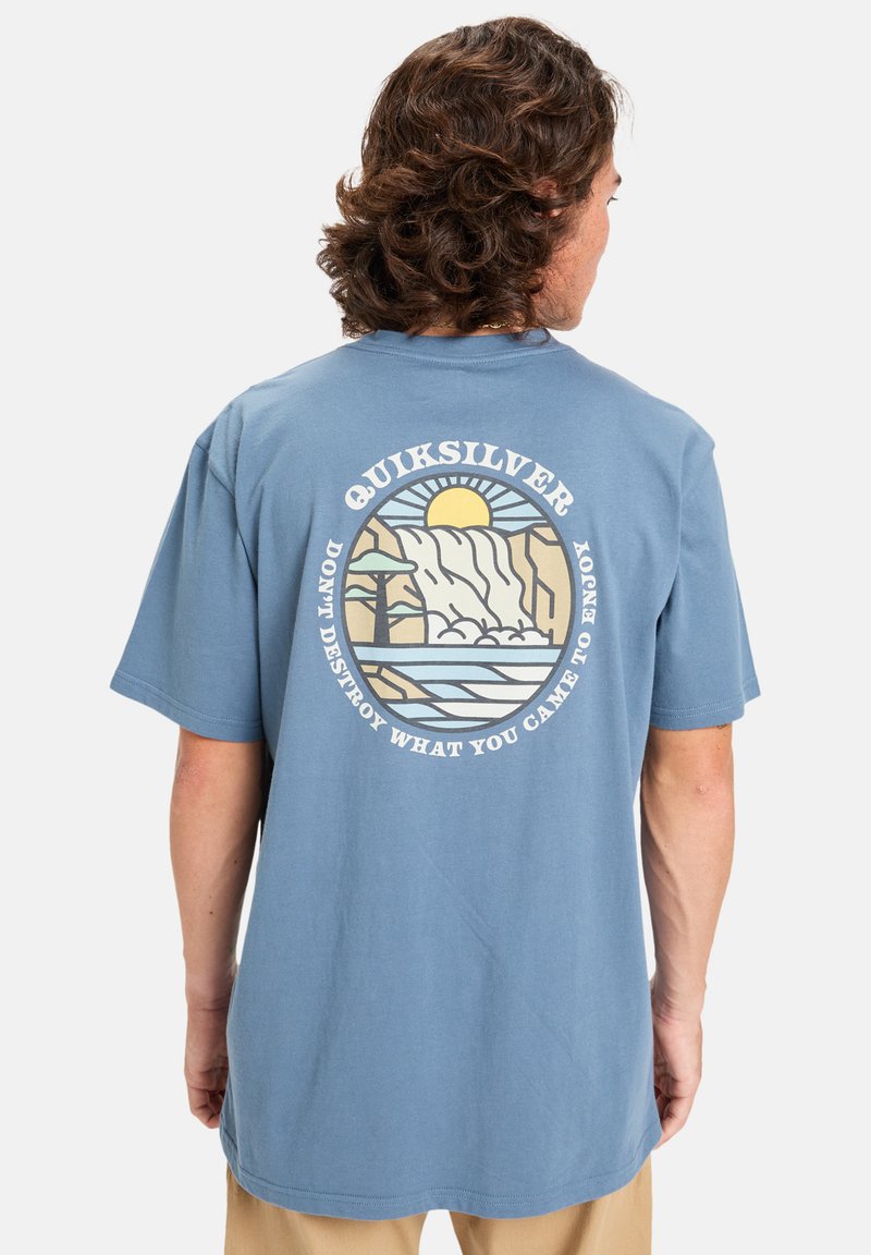 Modrá bavlněná tričko s barevným grafikou slunce, hor a vody, se textem "Quiksilver" a sloganem kolem designu.