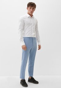 Weißes Hemd mit langen Ärmeln, kombiniert mit hellblauen maßgeschneiderten Hosen und schwarzen Sneakers, mit einer glatten Textur und schmaler Passform.