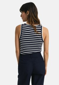 Marineblå og hvid stribet tanktop med rund halsudskæring og ærmeløs design. Bæres med mørke bukser, der fremhæver det glatte stof og den tætsiddende pasform.
